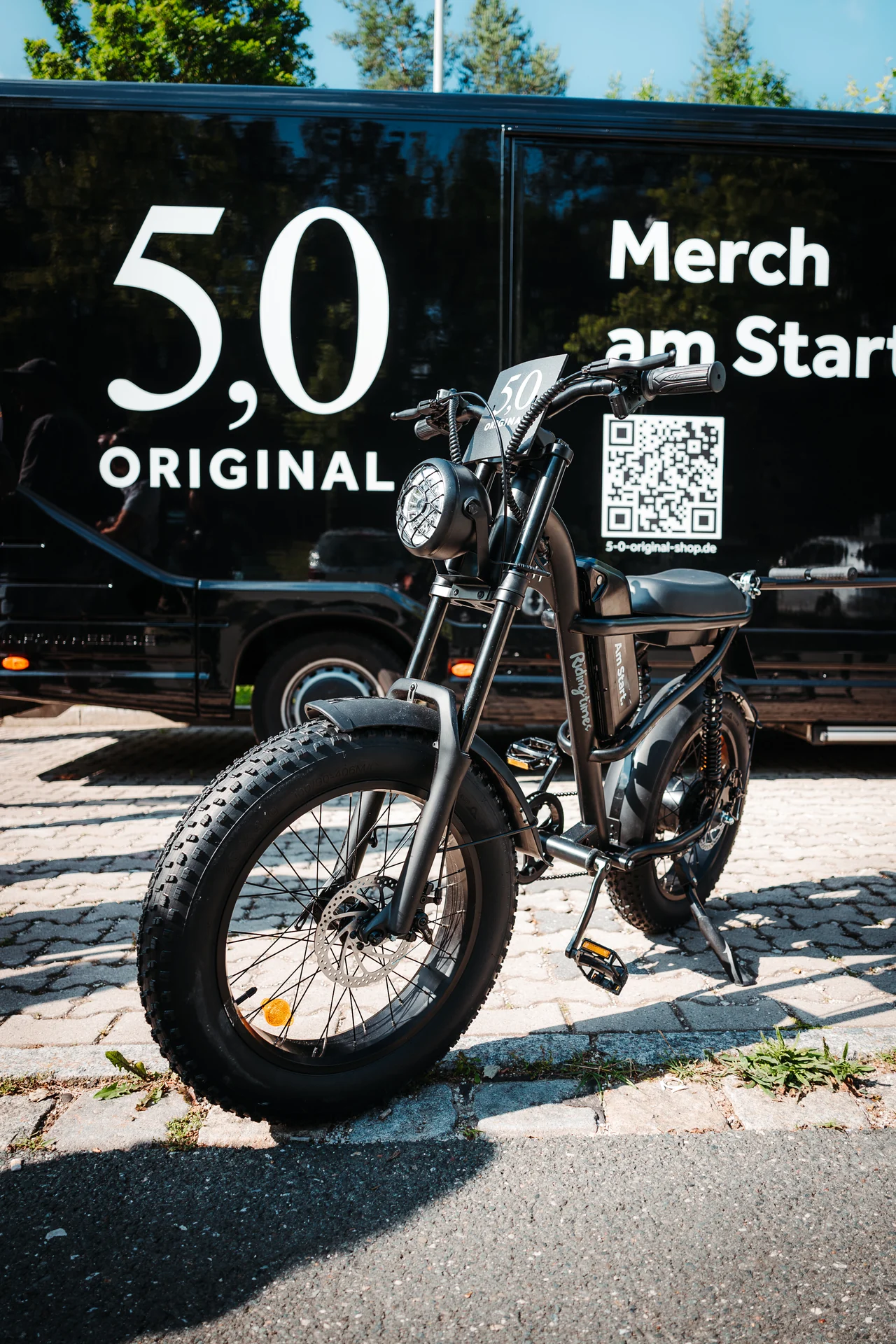 5,0 ORIGINAL MerchTruck und gebrandetes E-Bike auf einem Festivalgelände.