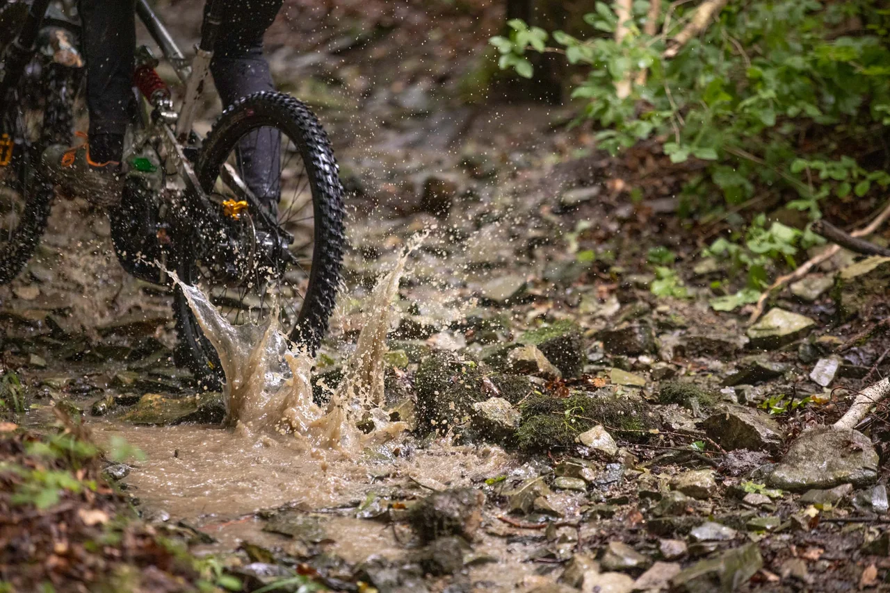 Das Hinterrad eines Mountainbikes spritzt durch Wasser auf einem steinigen Trail