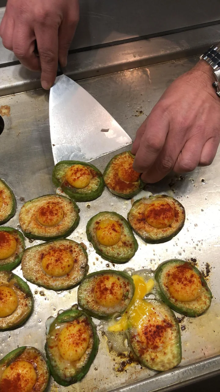 Hände schneiden gefüllte Avocadohälften auf einem Brett in der Küche.