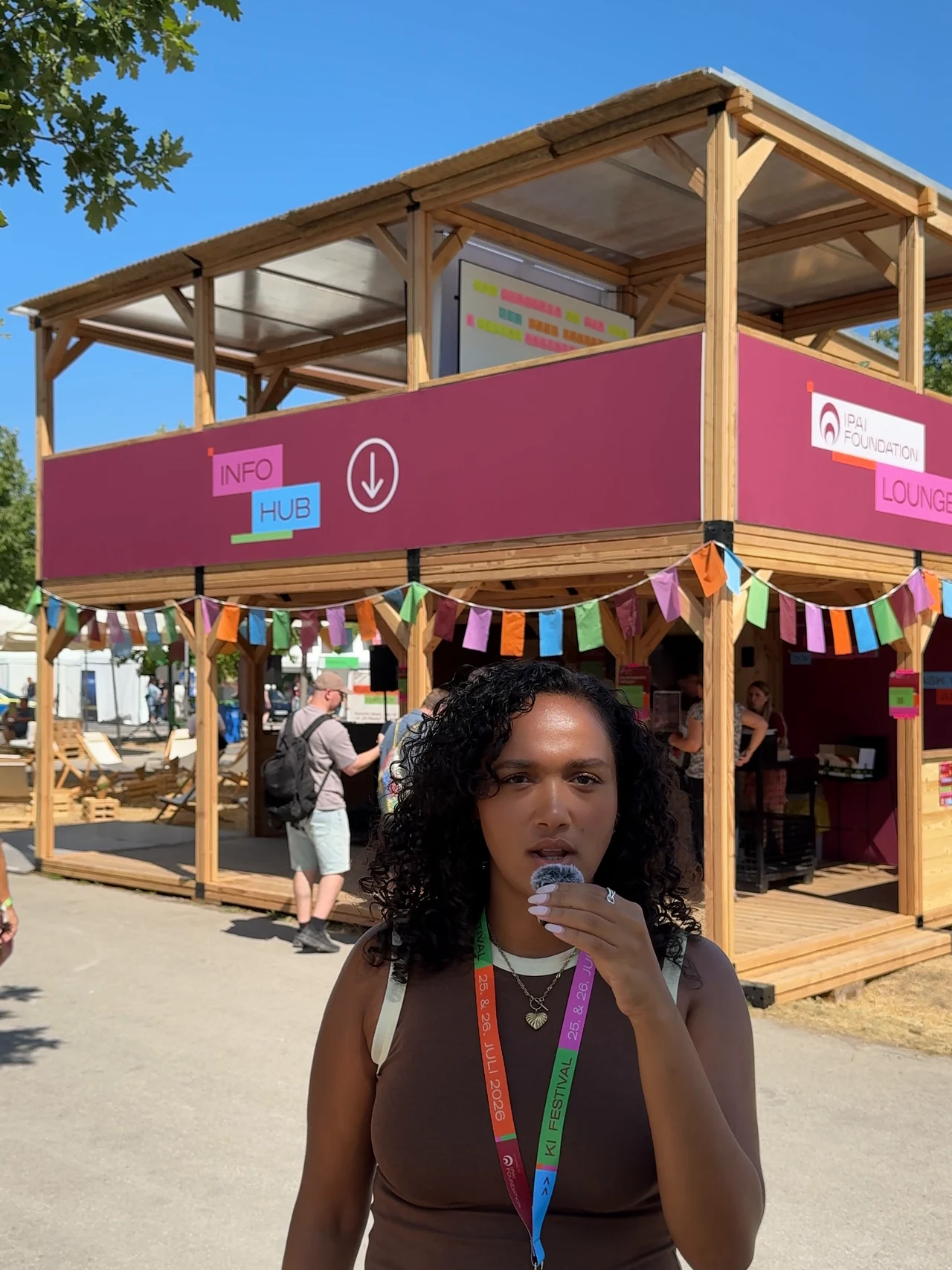 Person mit Mikrofon vor dem Infohub des KI-Festivals 2026.