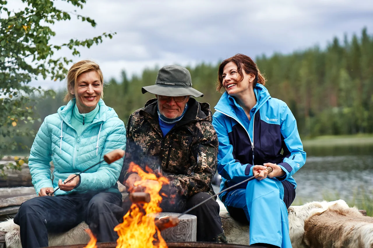 Menschen sitzen am Lagerfeuer in Outdoor-Bekleidung.